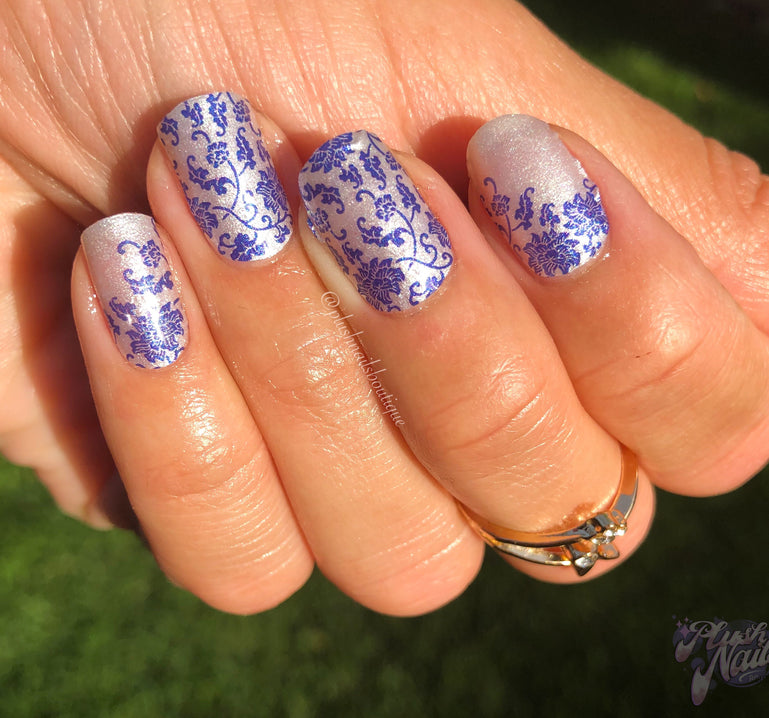 hand with white nail wraps with blue vine and flower design.